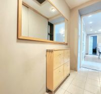 Der Flur in der 2-Zimmer-Wohnung mit Holzmöbeln, Fliesen und einem großen Spiegel.