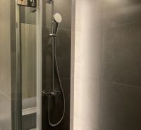 Duschkabine mit grauen Fliesen in einer Einzimmerwohnung.