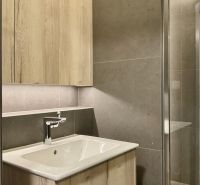 Badezimmer mit hellem Holzmöbel und dunklen Fliesen in einer Einzimmerwohnung.
