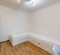 Ein Zimmer mit zwei Betten, weißen Möbeln und einem Boden in Holzoptik in einer 3-Zimmer-Wohnung.