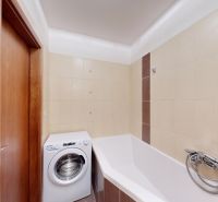 Badezimmer mit hellen Fliesen, Eckbadewanne und Waschmaschine in einer 3-Zimmer-Wohnung.