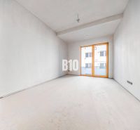 Ein leerer Raum mit Betonboden und großen Fenstern in einer 3-Zimmer-Wohnung.