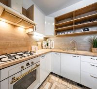 Küche in einer 2-Zimmer-Wohnung, helle Schränke, offene Regale, Boden mit Holzdekor.