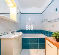 Badezimmer mit Badewanne und Waschbecken in einer 2-Zimmer-Wohnung mit blau-weißen Fliesen.