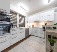 Eine Küche in einem Einfamilienhaus mit weißen Schränken und einem Fenster mit Jalousien.