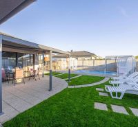 Ein Einfamilienhaus in Most pri Bratislave mit Terrasse, Pool und Liegestühlen auf dem Rasen.
