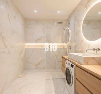 Badezimmer in einer 4-Zimmer-Wohnung mit großer Dusche, Waschmaschine und beleuchtetem Spiegel.
