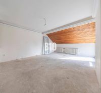 Ein unmöbliertes Zimmer mit einem Heizkörper und einer Holzdecke im Dachgeschoss eines Einfamilienhauses.