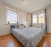 Helles Schlafzimmer mit Bett, großen Fenstern und Holzboden in einer 2-Zimmer-Wohnung.