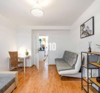 Wohnzimmer in einer Zweizimmerwohnung mit Holzboden und einfacher Einrichtung.