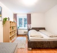 Schlafzimmer in einer 2-Zimmer-Wohnung mit Bett, Regal, Fenster und Boden in Holzoptik.