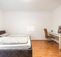 Schlafzimmer in einer 2-Zimmer-Wohnung mit Bett, Tisch und Boden in Holzoptik.