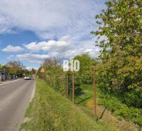 Straße in Dunajská Lužná mit Grundstücken für Wohnzwecke, umgeben von Grünflächen und einem Zaun.