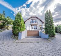 Einfamilienhaus in Marianka mit Strauchumrandung, Garage und teilweise bewölktem Himmel.