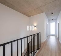 Ein Flur mit Betondecke, Holzboden und Treppe in einem Einfamilienhaus.