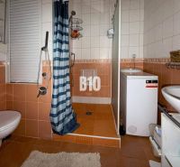 Badezimmer in einer 3-Zimmer-Wohnung mit orangefarbenen Fliesen, Dusche, Waschmaschine und WC.