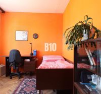Zimmer in einer 3-Zimmer-Wohnung mit Ausstattung: Bett, Tisch, Regal und Heimtrainer.