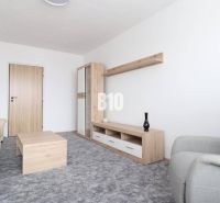 Wohnzimmer mit beigem Sofa, grauem Sessel und Möbeln mit Holzdekor in einer 3-Zimmer-Wohnung.