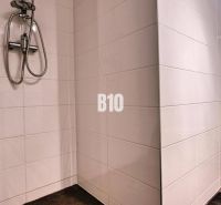 Badezimmer in einer 3-Zimmer-Wohnung mit weißen Fliesen, Dusche und Toilette.