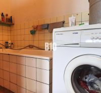 Badezimmer in einem Einfamilienhaus mit Badewanne, Waschmaschine und Reinigungsmitteln auf dem Regal.