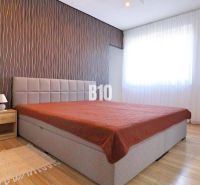 Schlafzimmer mit Bett, Tapetenwand, Holzdekorboden und Möbeln in einem Einfamilienhaus.