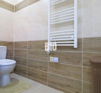 Badezimmer mit Toilette, Fliesen mit Holzdekor, Heizkörper, Korb, Boden mit Holzdekor.