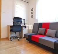 Ein Zimmer eines Einfamilienhauses mit einem Schreibtisch, einem Stuhl und einem bunten Sofa, Boden mit Holzdekor.