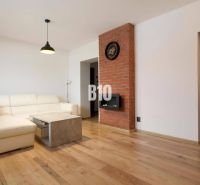Wohnzimmer in einer 3-Zimmer-Wohnung mit weißem Sofa, Ziegelwand und Holzboden.