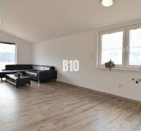 Wohnzimmer in einem Einfamilienhaus, helle Couch, Boden mit Holzdekor, große Fenster.
