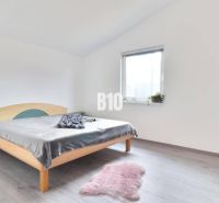 Helles Schlafzimmer im Einfamilienhaus mit Bett, Teppich und Boden in Holzoptik.