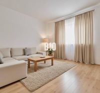 Wohnzimmer eines Einfamilienhauses mit beigem Sofa, Couchtisch und Boden in Holzoptik.