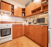 Eine Küche mit Holzschränken, weißen Geräten und einem Boden in Holzoptik in einer 2-Zimmer-Wohnung.