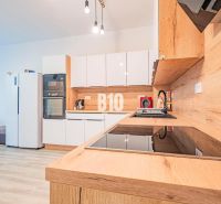 Küche in einer 3-Zimmer-Wohnung mit glänzenden weißen Schränken und einem Boden in Holzoptik.