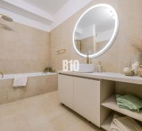 Badezimmer in einer 2-Zimmer-Wohnung mit Badewanne, rundem Spiegel und beigen Fliesen.
