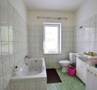 Ein Badezimmer in einem Einfamilienhaus mit einer Badewanne, einem Waschbecken und einer Waschmaschine, gefliest mit hellen Fliesen.