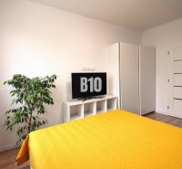 Schlafzimmer in einer 3-Zimmer-Wohnung mit Fernseher, Schrank und Boden in Holzoptik.