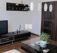 Wohnzimmer mit Fernseher, Regalen, Tisch und Holzboden in einer Vierzimmerwohnung.