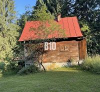 Eine Holzhütte in Kunerad mit rotem Dach, umgeben von Wäldern und Wiesen.