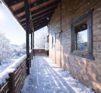 Die verschneite Terrasse einer Holzhütte in Bytča mit Blick auf die Winterlandschaft.