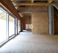 Unvollendetes Interieur eines Einfamilienhauses mit großen Fenstern und Ziegelwänden.