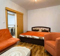 Ein Zimmer mit einem Doppelbett, einem orangefarbenen Sessel und einem Boden in Holzoptik.