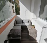 Ein verglaster Balkon mit Rattanmöbeln und einem Boden in Holzoptik in einer Einzimmerwohnung.