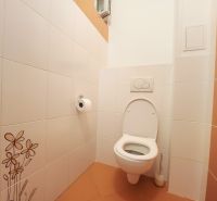 Toilette mit weißen Fliesen und orangefarbenen Bodenfliesen in einer 3-Zimmer-Wohnung.