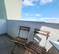 Balkon einer 3-Zimmer-Wohnung mit zwei Holzstühlen, blauem Himmel und Schutznetz.