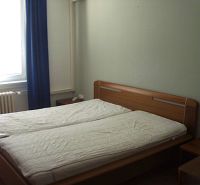 Schlafzimmer in einer 2-Zimmer-Wohnung mit Ehebett, Fenster und Vorhang.