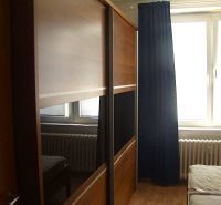 Ein Schrank mit Schiebetüren, ein Bett und ein Heizkörper im Schlafzimmer einer Zweizimmerwohnung.