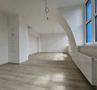 Geräumiges Wohnzimmer mit Holzboden und großen Fenstern in einer Einzimmerwohnung.