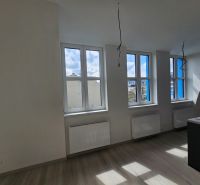 Helles Zimmer mit drei Fenstern und Holzboden in einer Einzimmerwohnung.