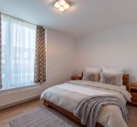Schlafzimmer mit großem Fenster, Doppelbett und Holzboden in einer Zweizimmerwohnung.
