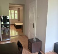 Innenraum einer 2-Zimmer-Wohnung mit Holzboden, Sitzbereich und Eingang zum Schlafzimmer.